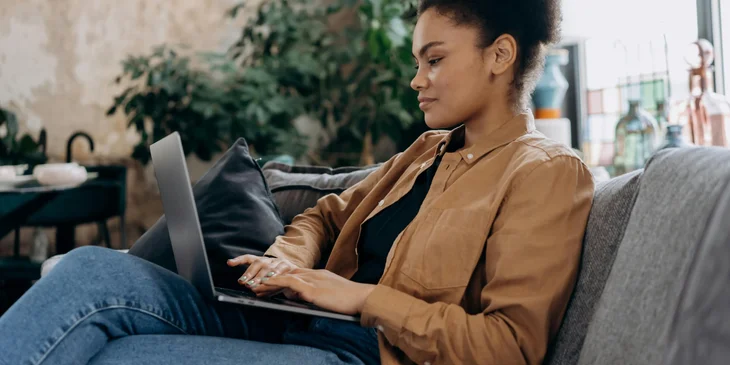 A woman is sitting on the couch, working on her laptop.