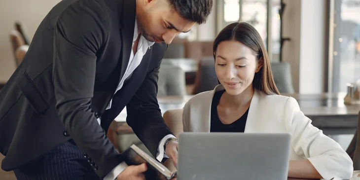 A man helping his coworker with her work on the laptop.