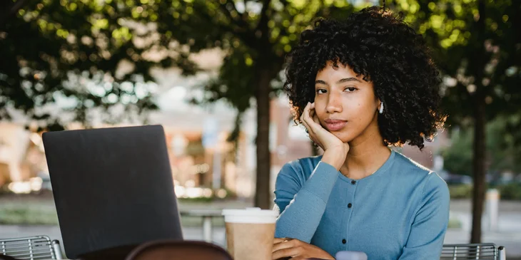 A woman drinking coffee while working on her laptop outdoors.