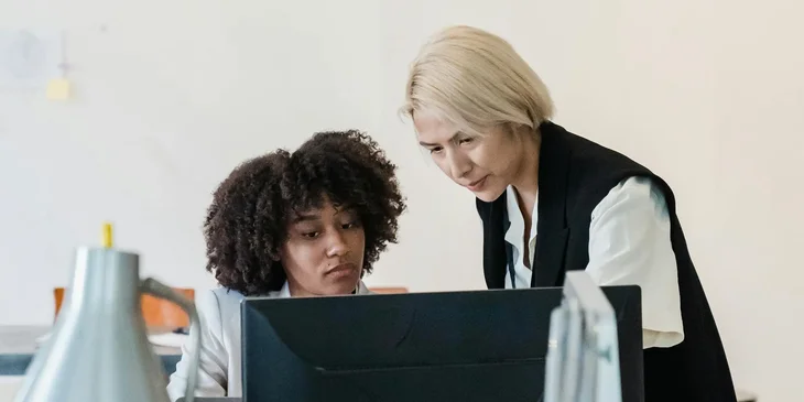 Two coworkers discussing a project by a computer.