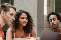 Drei Studierende arbeiten auf einem Laptop.