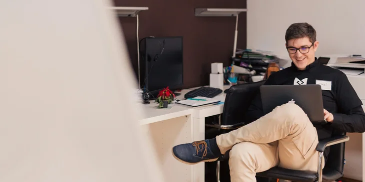 A man sitting in an office chair, working on his laptop.