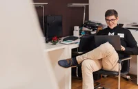 A man sitting in an office chair, working on his laptop.