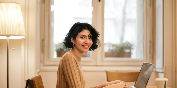 A happy journalist sitting in a cafe in front of her laptop.