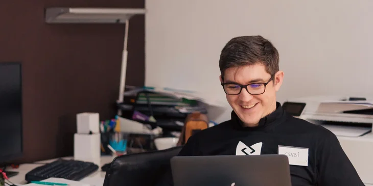 İş yerinde laptop kullanırken gülümseyen bir adam.