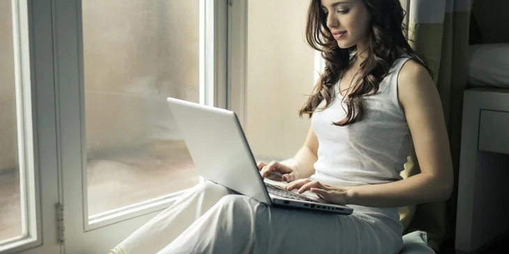 A woman wearing a tank top sitting by the window.