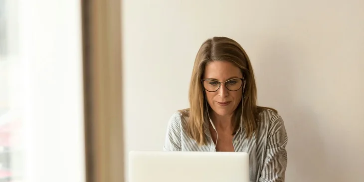 A woman wearing grey striped dress shirt sitting in front of a white laptop.