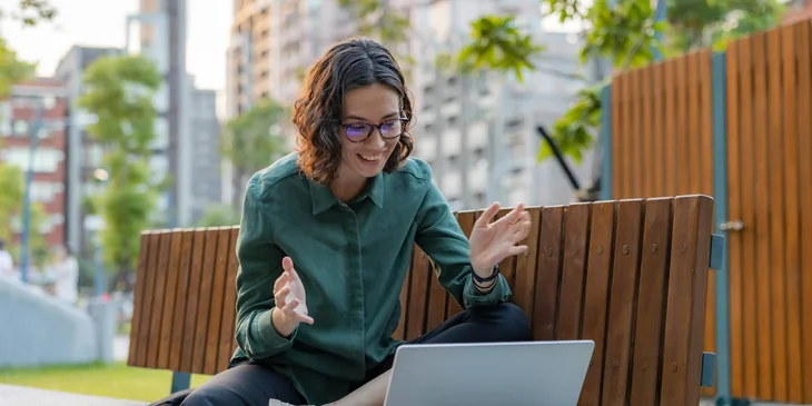 A woman happily working remotely at a park bench.