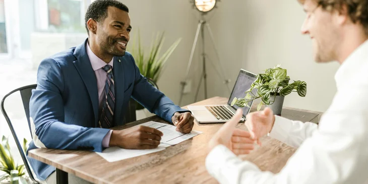 A male life insurance agent in a black suit discussing the best plan for his client.