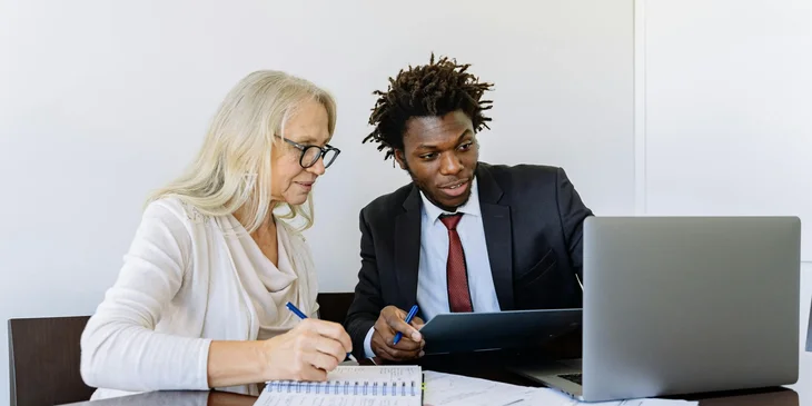 A loan specialist sitting next to a woman in a white shirt, discussing a loan option.
