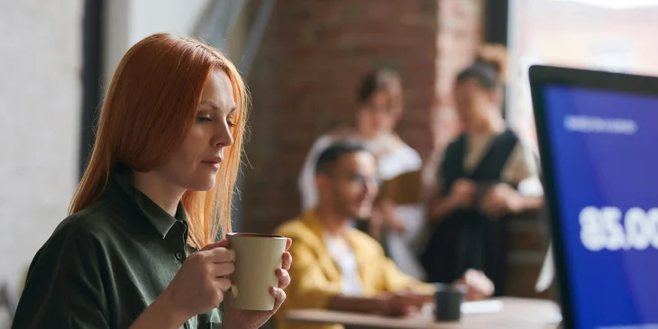 A woman holding a coffee mug while working at her desk.