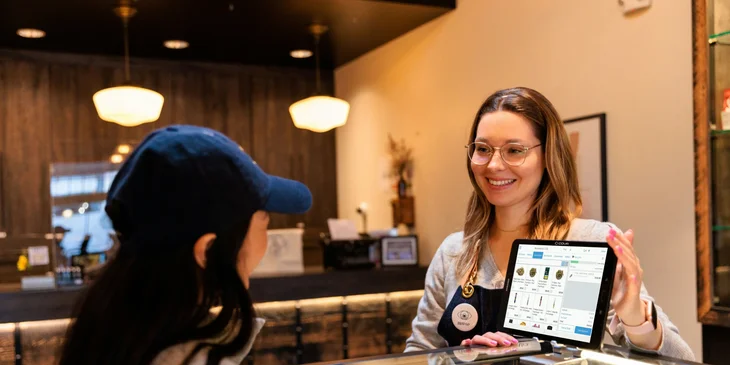 A cheerful budtender showing different varieties of buds to a customer.
