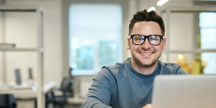 A person wearing glasses sits at a desk.