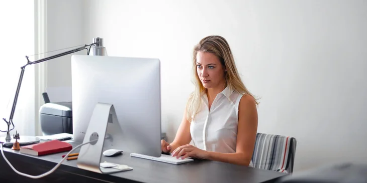 A woman in white sleeveless shirt using a computer.
