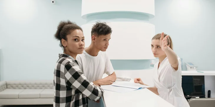 A medical receptionist guiding the patient and their guardian to the doctor's office.