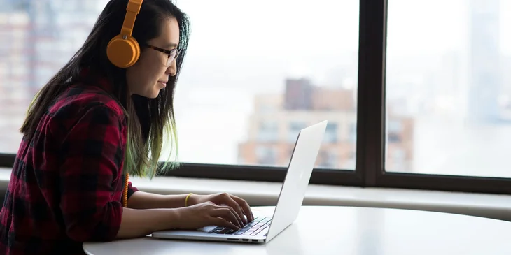 A medical transcriptionist typing on a laptop while listening through headphones.