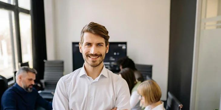 A man standing in a meeting room with his team in the background.