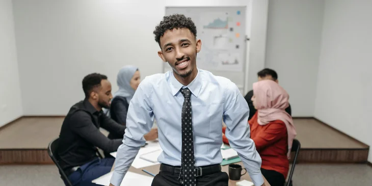 A man sitting on an office table with his team in the background.