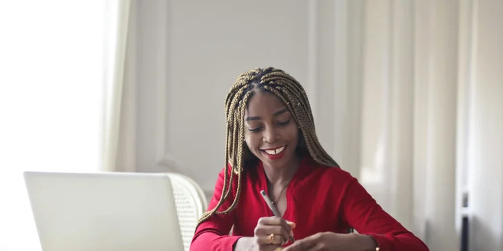A woman sitting in front of a laptop and writing on a pad.