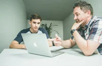 Un entrevistador sentado frente a su laptop y al lado de un entrevistado.