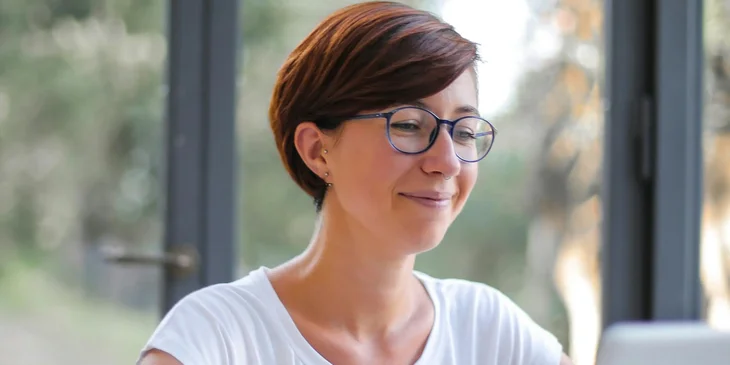 A woman in white crew neck T-shirt wearing a black framed glasses.