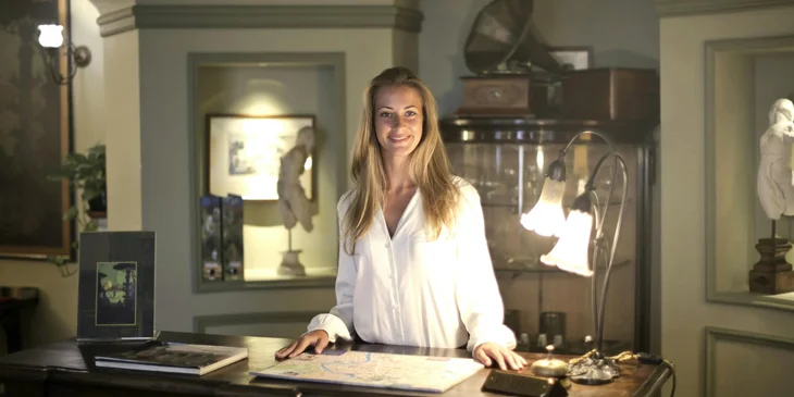 A female night auditor stands in the reception area, warmly smiling at the arriving guests.
