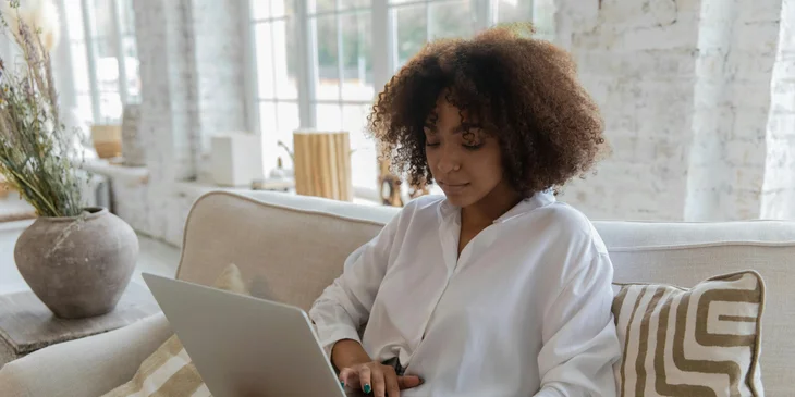 A woman sitting on a couch, working on her laptop.