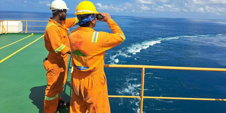 Workers on a ship's platform surveying the sea.