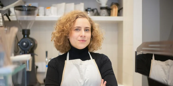 A woman wearing an apron working in a coffee shop.