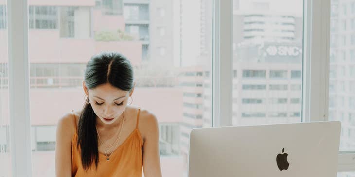 A woman working at her office desk with a computer screen and office plant.