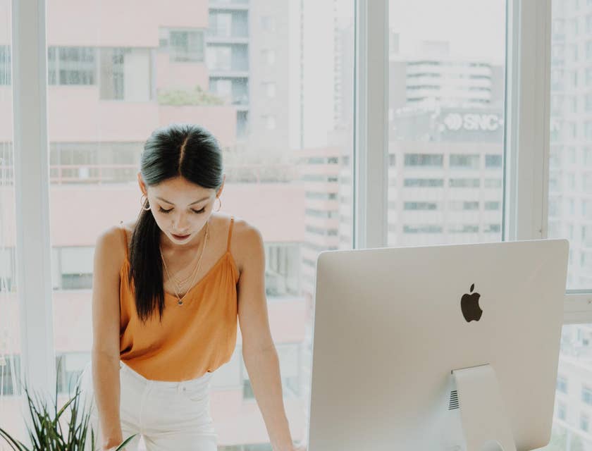 A woman working at her office desk with a computer screen and office plant.