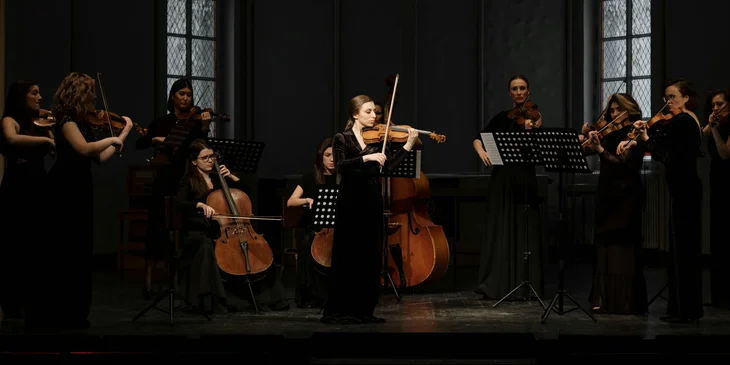 A group of women playing string instruments as part of an orchestra.
