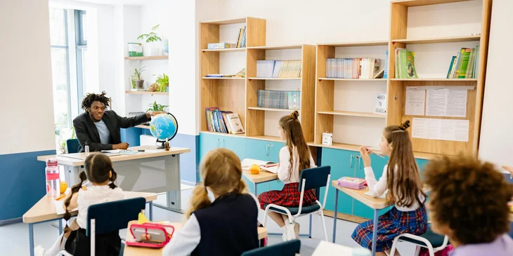 A teacher sitting in front of a class showing a globe.
