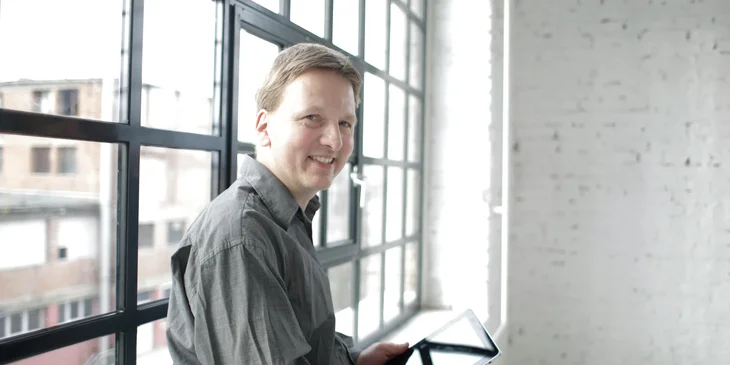 A man standing by the window of a building.