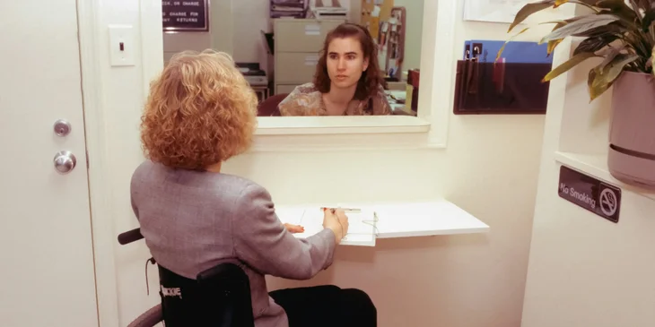 A patient care coordinator speaks with a patient in a wheelchair.