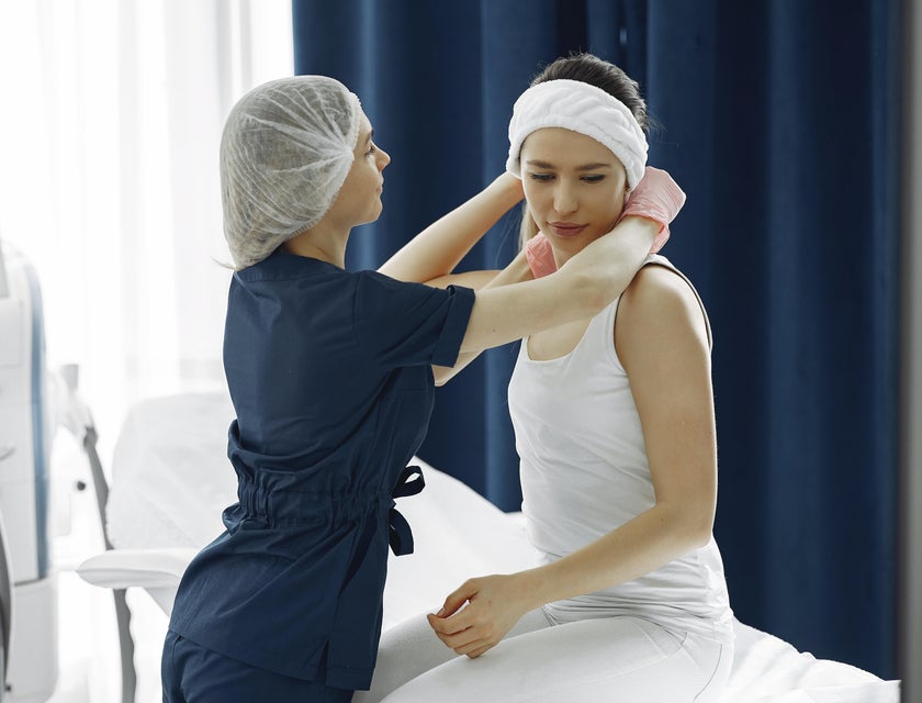 A patient services technician helping a patient to sit up and placing a cloth around her neck.