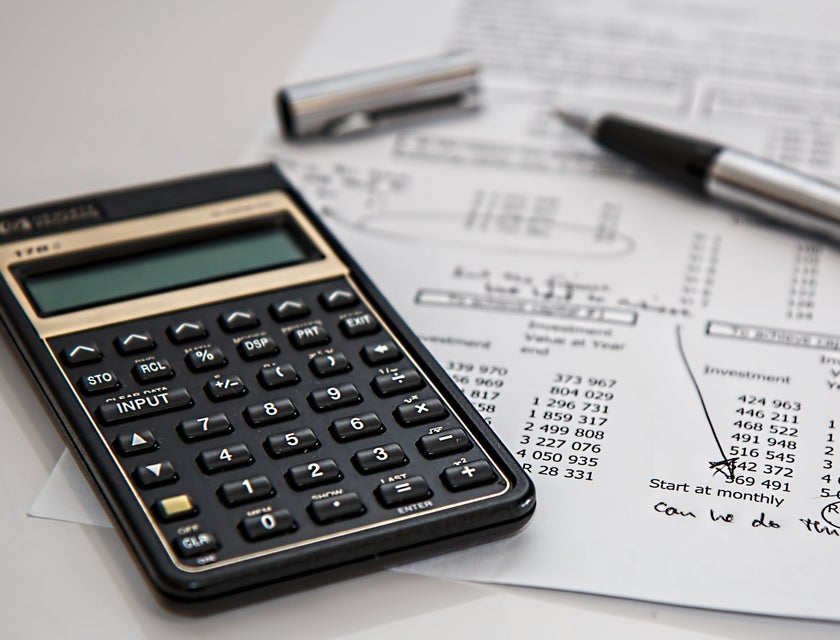 Calculator, financial documents, and a pen on the desk of a payroll staff member.
