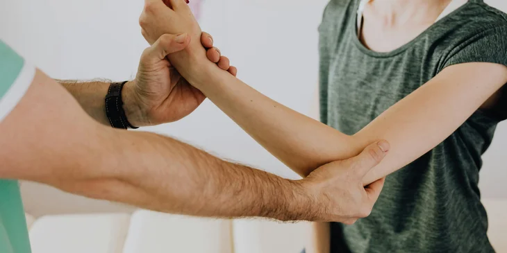 A physical therapy aide carefully stretches the patient's arm.