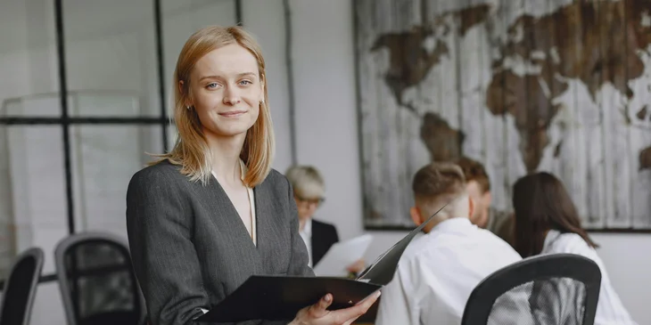 A woman holding a folder stands by the office desk.