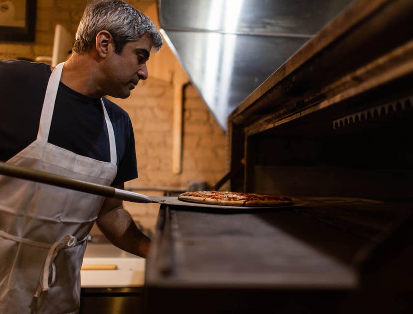 A pizza maker putting a pizza into an oven.