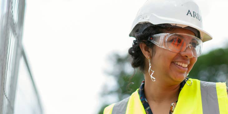 Una ingeniera usando un casco blanco y un chaleco amarillo mientras trabaja.