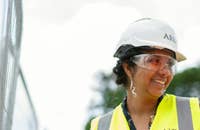 Una ingeniera usando un casco blanco y un chaleco amarillo mientras trabaja.