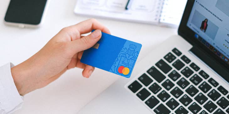hand holding credit card above laptop.