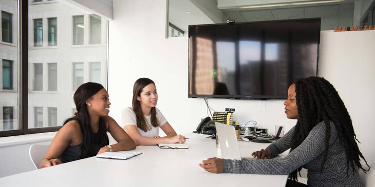Mujeres sentadas en un escritorio blanco en una oficina de una empresa.