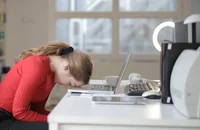 Una empleada vestida de rojo y negro con su cabeza recargada sobre su escritorio.
