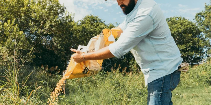 A man in white shirt and blue denim jeans holding a brown textile.
