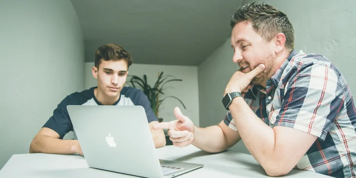 An interviewer sitting in front of his laptop and next to an interviewee.