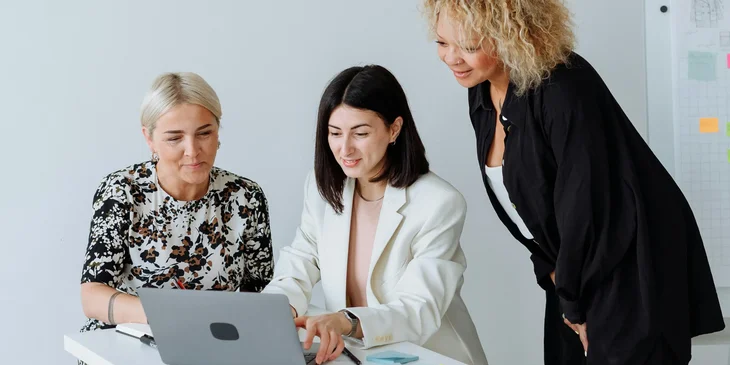 A women beside a white table looking at a laptop.