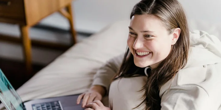 Eine lächelnde Person, die zu Hause auf ihrem Laptop arbeitet.
