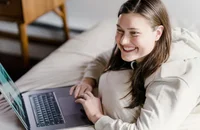 Eine lächelnde Person, die zu Hause auf ihrem Laptop arbeitet.